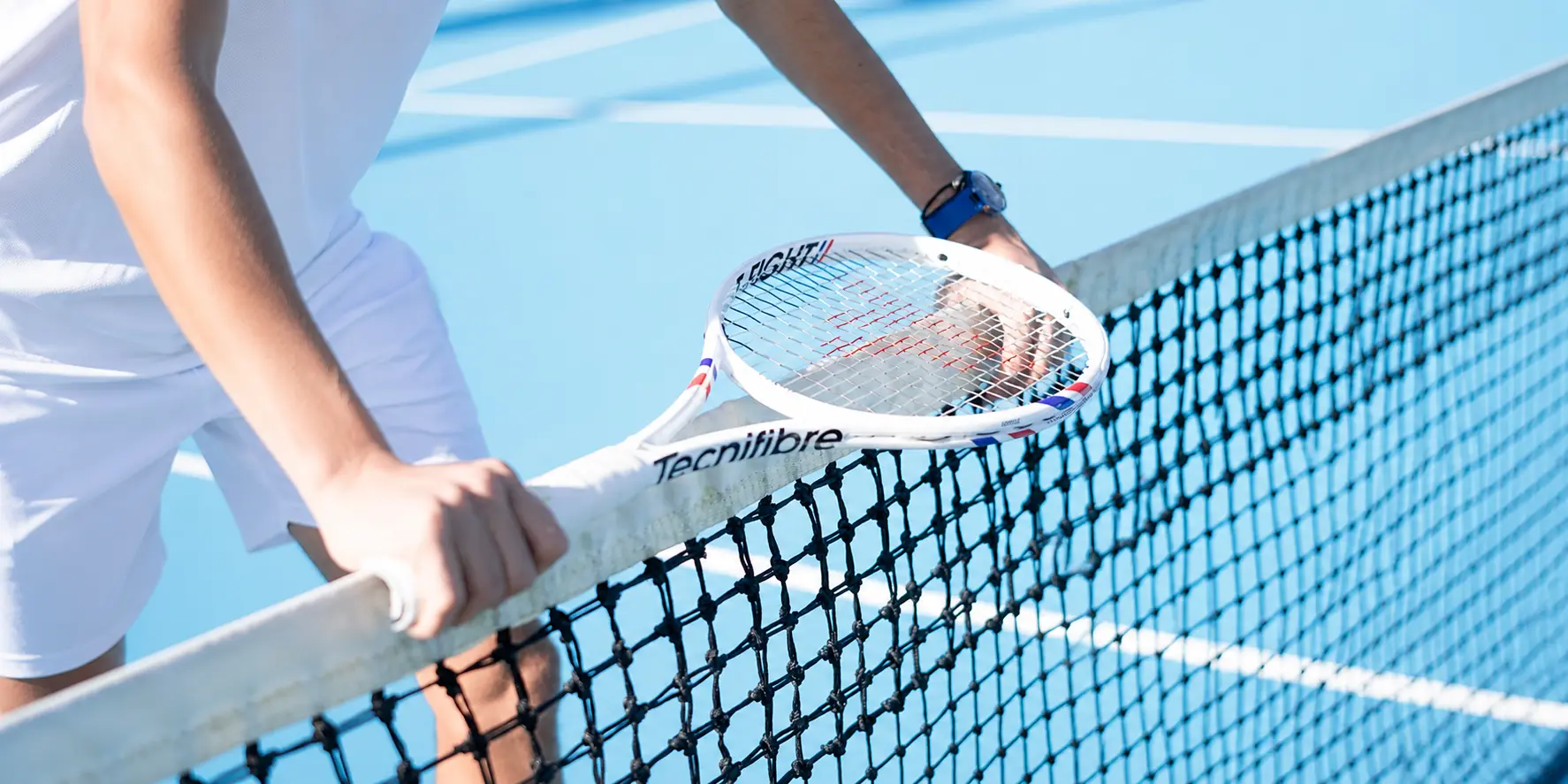 Tecnifibre T-Fight racket resting against the net on a blue hard court